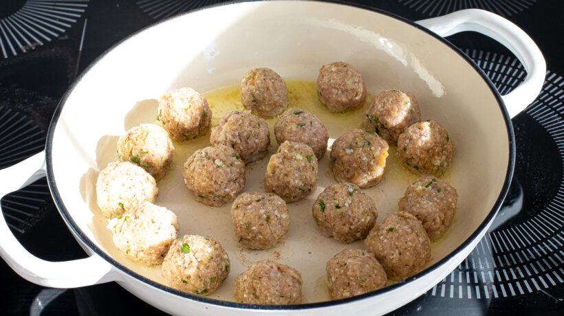 Chicken meatballs being cooked in a white skillet on the stove.