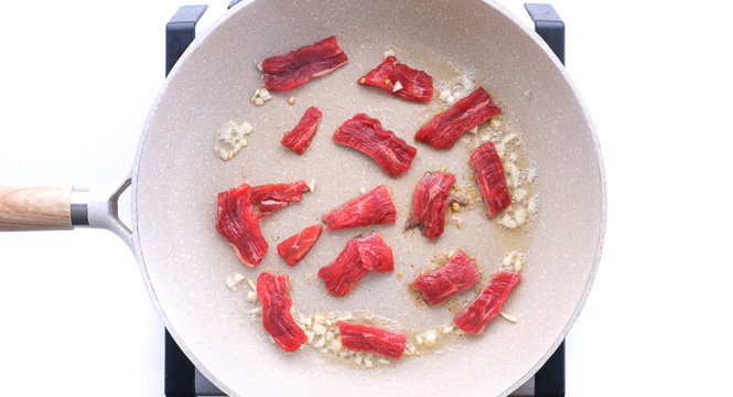 searing flank steak and garlic in skillet