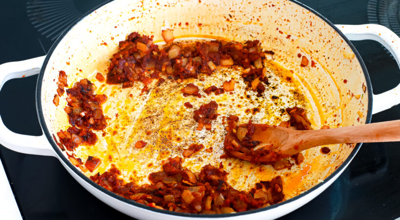 Tomato paste, onions and calabrian chiles cooking in a skillet. 