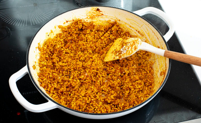 Turmeric rice stirred by a spatula in a large skillet.