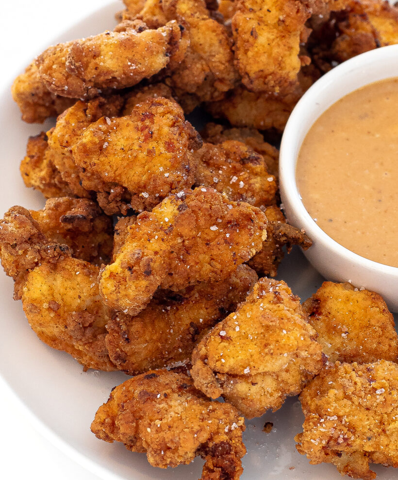 Chicken nuggets on a white plate with a small white bowl of sauce on the plate.
