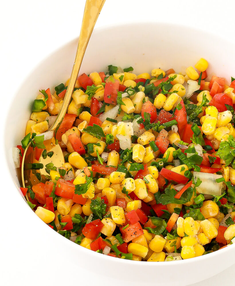 White bowl full of corn salsa with a spoon on the side. 