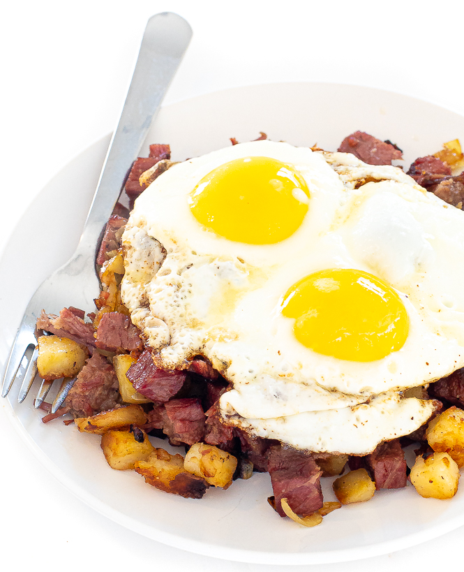 Corned beef hash on a white plate with two fried eggs on top.