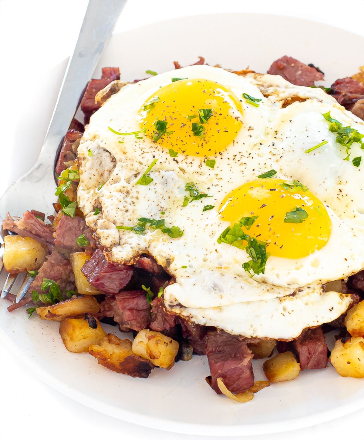 Two fried eggs on top of potatoes and beef in a white bowl.