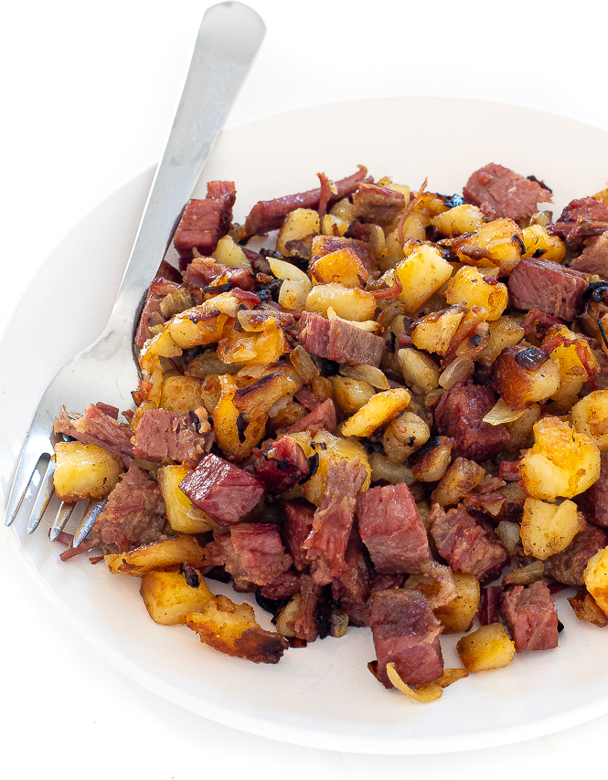 Corned beef hash on a white plate with a silver fork.