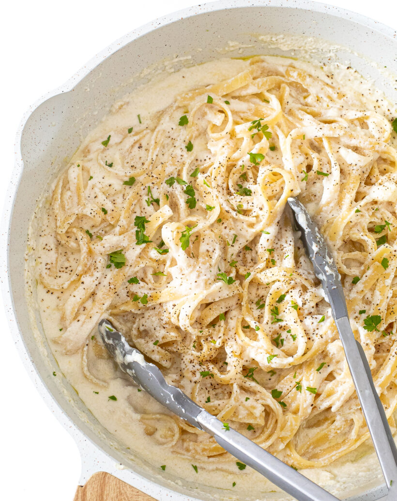 Cottage cheese alfredo topped with black pepper and parsley in a white skillet with tongs.