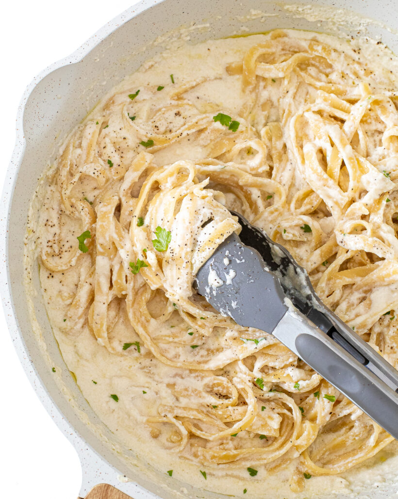 Tongs grabbing cottage cheese alfredo in a white skillet.
