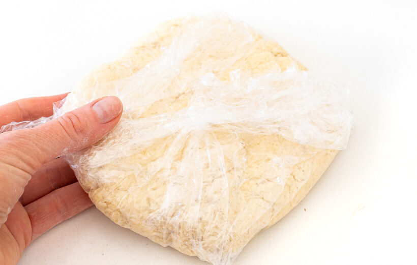 Cracker dough wrapped with plastic wrap. A hand is holding the dough.