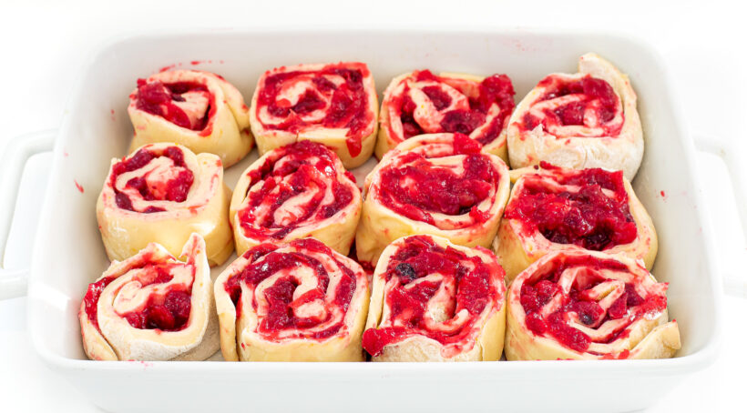 Sliced rolls with cranberry filling into a white baking dish.