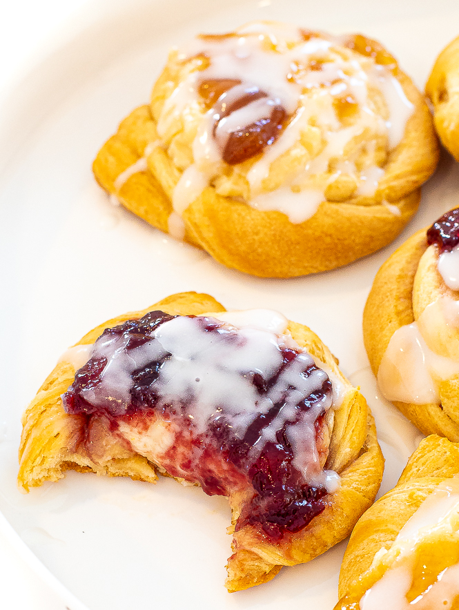 Danishes placed on a white plate with one that has a bite taken out of it. 