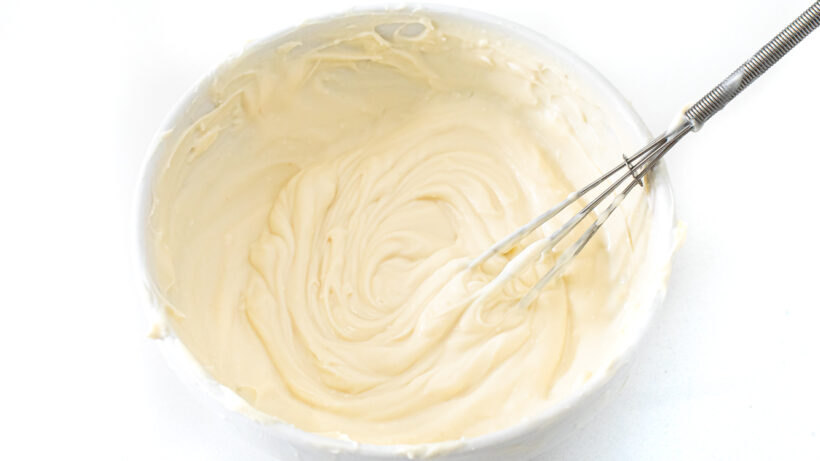 Healthier cream cheese frosting in a bowl with a whisk. 