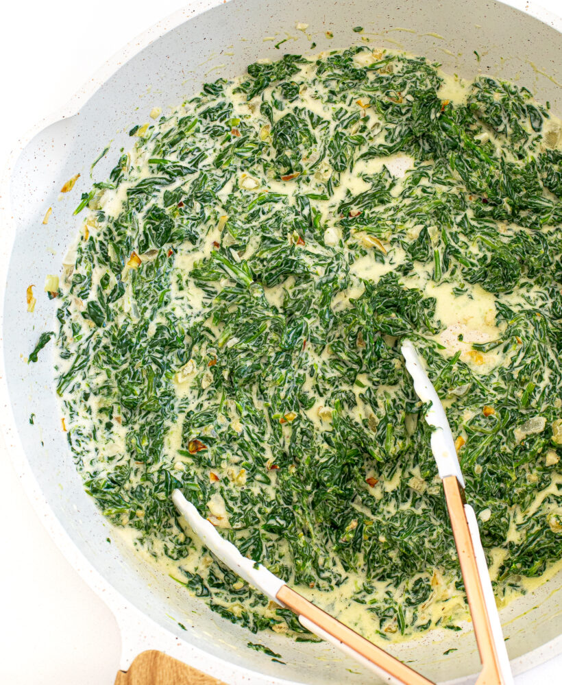 Overhead shot of creamed spinac in a skillet with tongs. 
