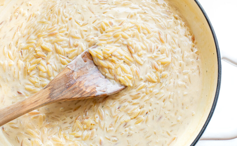 Creamy boursin orzo in a skillet with a wooden spoon.