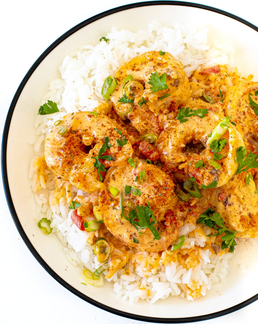 Creamy Cajun Shrimp topped with parsley and green onions on a plate of white rice.