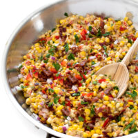 Homemade Confetti Corn with onion, peppers, and bacon in a skillet with a wooden serving spoon | chefsavvy.com