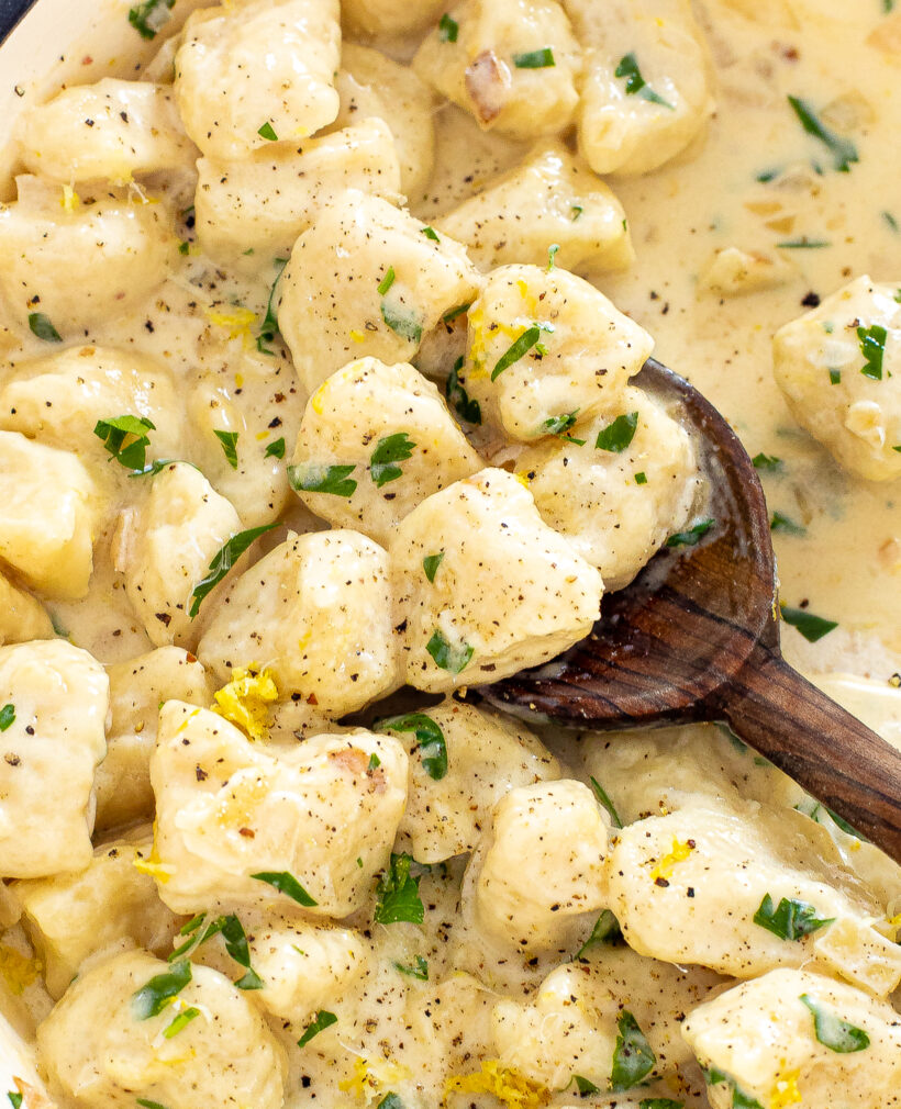 Close up shot of lemon gnocchi in a pan with a wooden spoon scooping some up. 