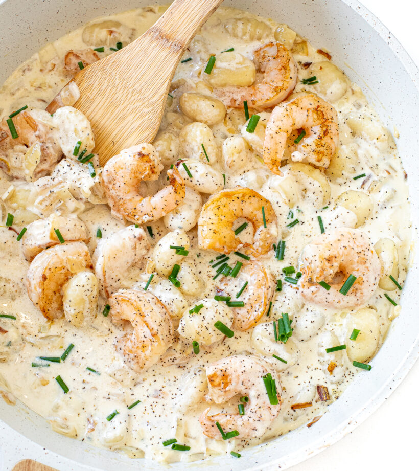 Gorgonzola gnocchi with shrimp in a skillet topped with chopped chives.