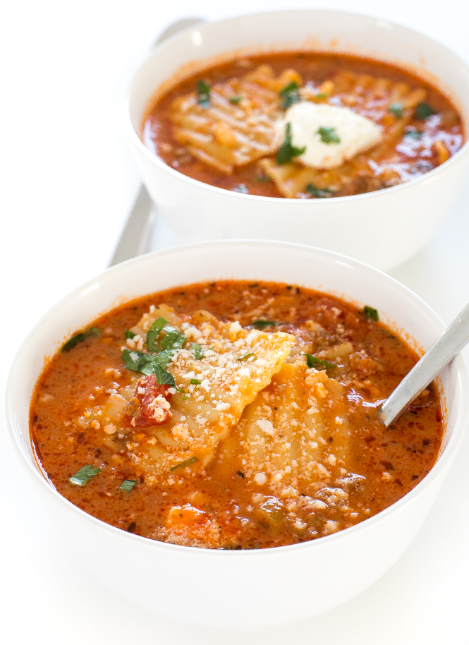 top shot of lasagna noodles in red broth served in two white bowls with spoons