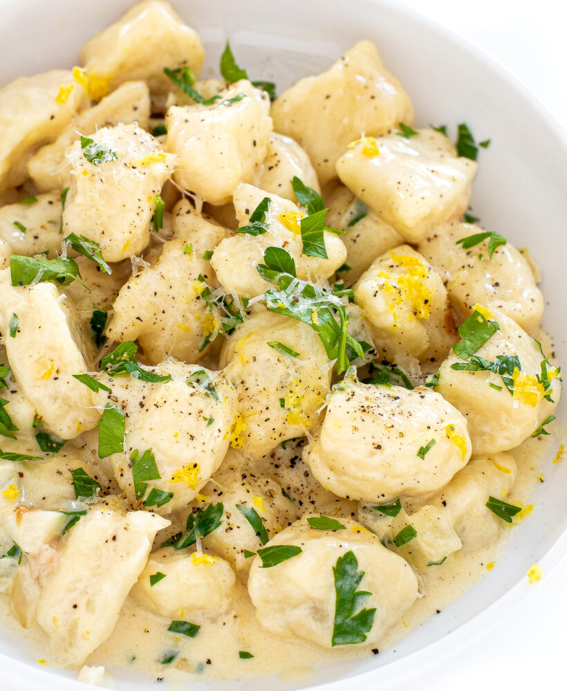Lemon parmesan gnocchi in a white bowl topped with parsley and parmesan. 