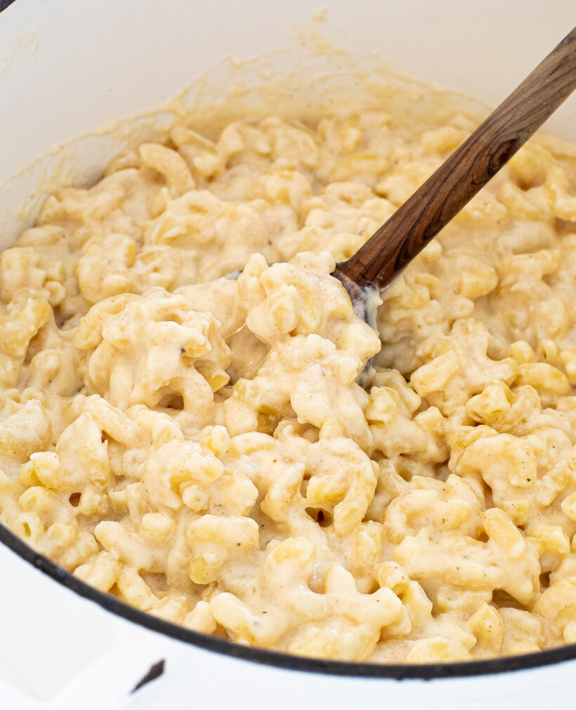 Three cheese mac and cheese in a large pan with a wood spoon.