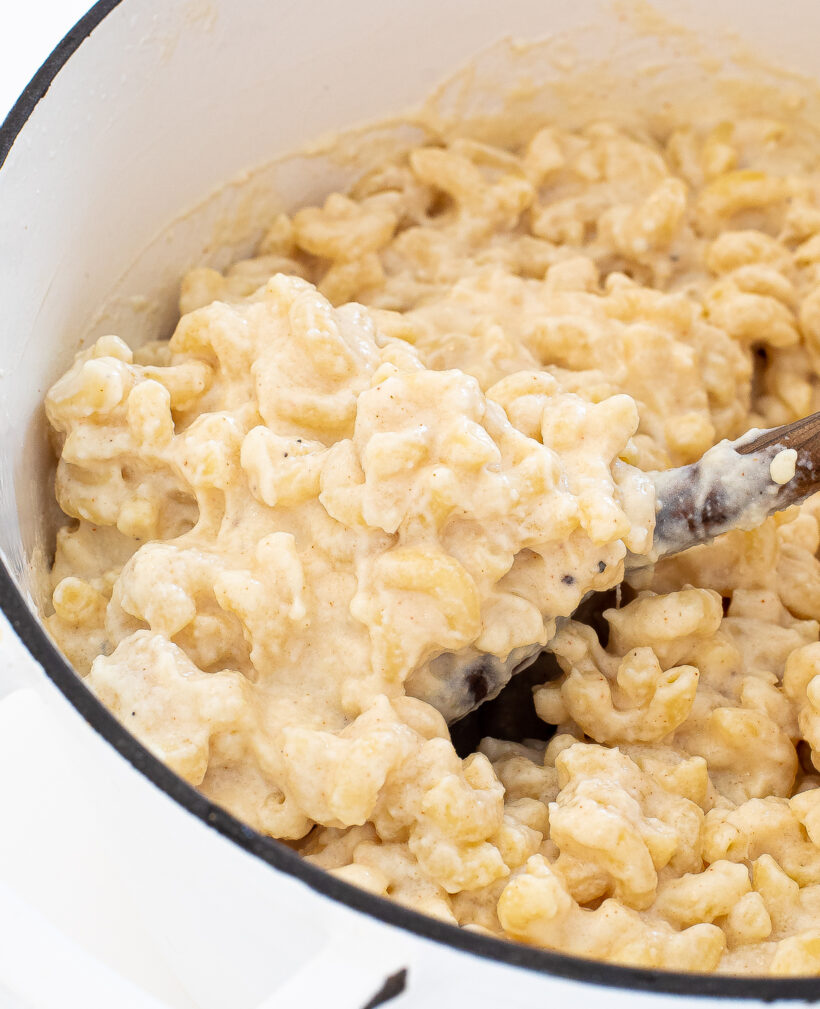 Three cheese mac and cheese in a pot with a wood spoon scooping some out.