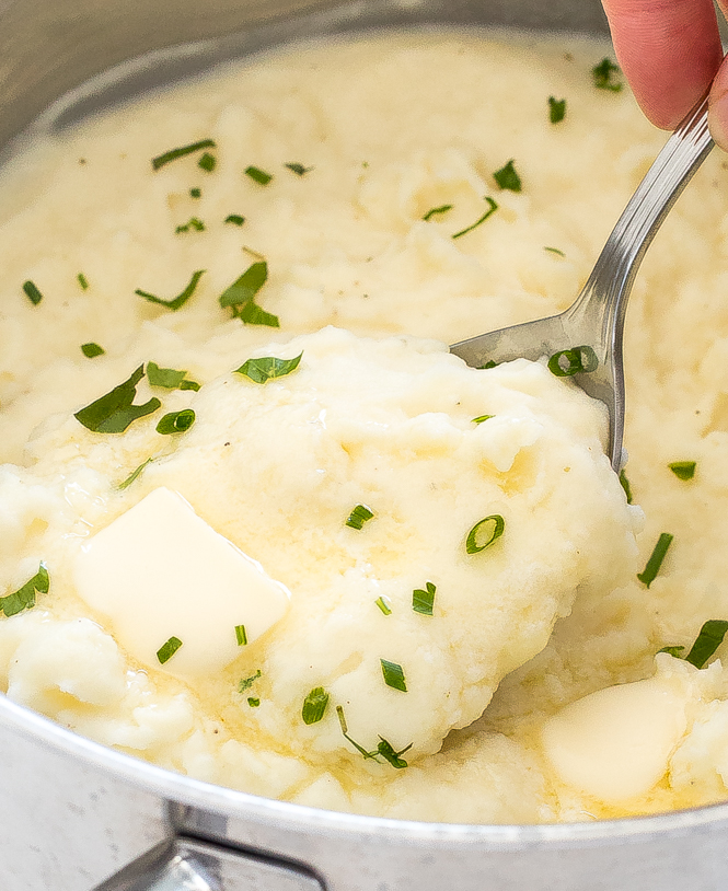mashed potatoes in a large pot topped with melted butter and chopped parsley