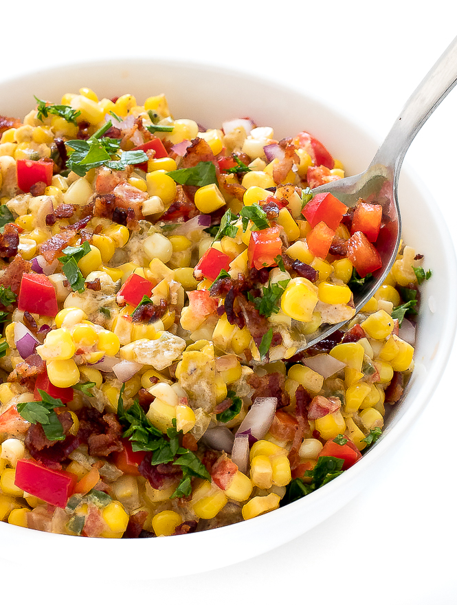 Homemade Confetti Corn with onion, peppers, and bacon in a white bowl with a metal spoon.