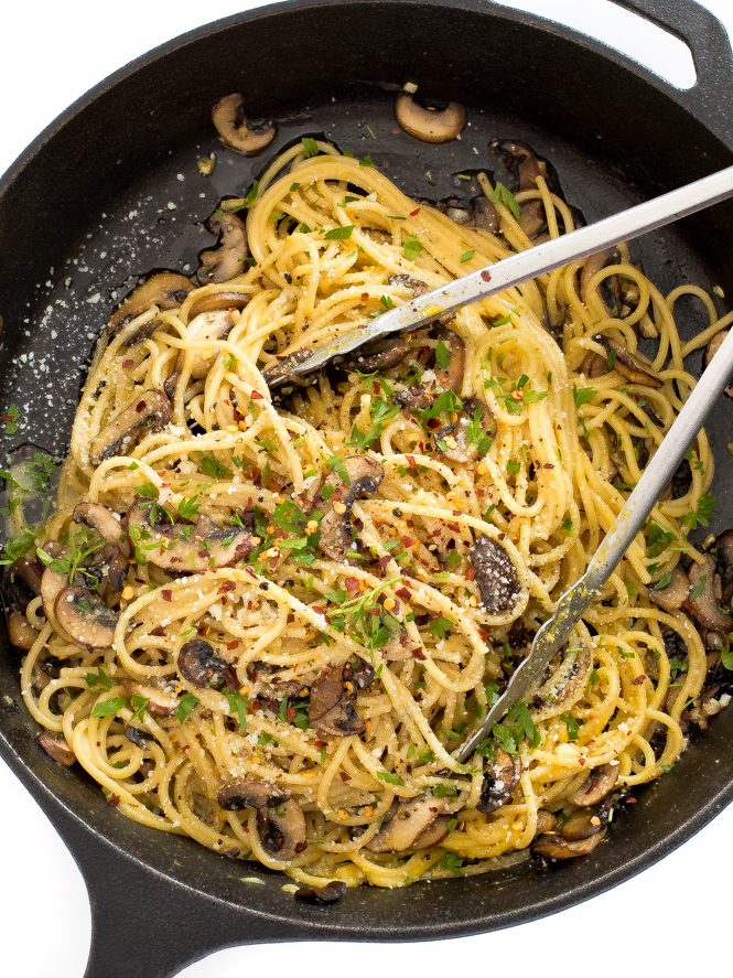 Top view of noodles with mushrooms in a pan with tongs. 