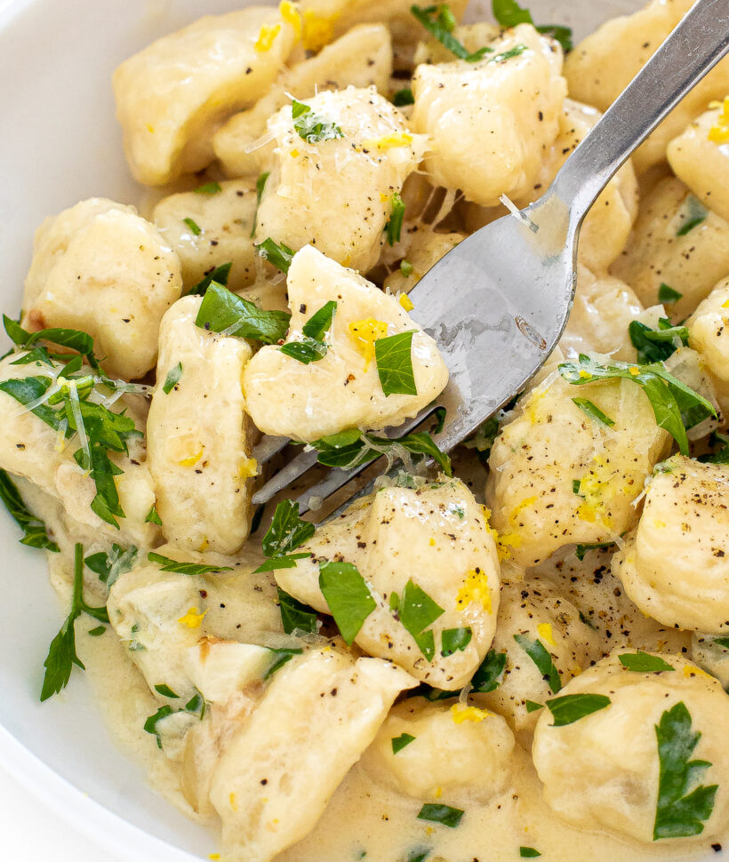 Fork scooping up a bite of lemon parmesan gnocchi from a bowl. 