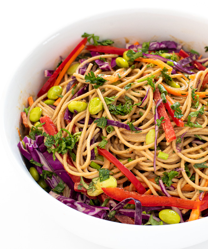 Noodles in a white bowl with veggies and a peanut sauce.