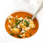 Creamy Roasted Red Pepper and Tomato Soup in a white bowl garnished with croutons, parsley, and feta cheese | chefsavvy.com