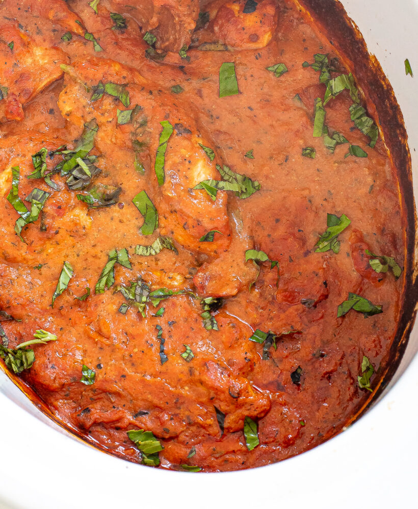 Chicken breast in a tomato sauce in a slow cooker with basil sprinkled on top.
