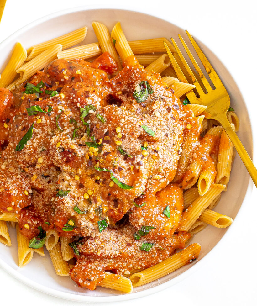 Slow cooker tomato basil chicken served on a bed of penne pasta.