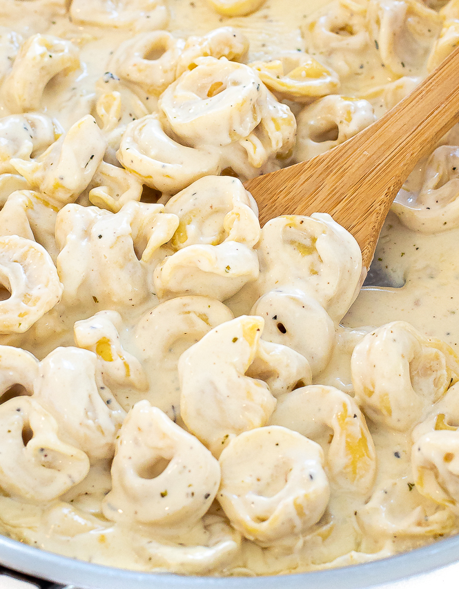 Tortellini in a silver sauce pan being stirred with a wooden spoon.