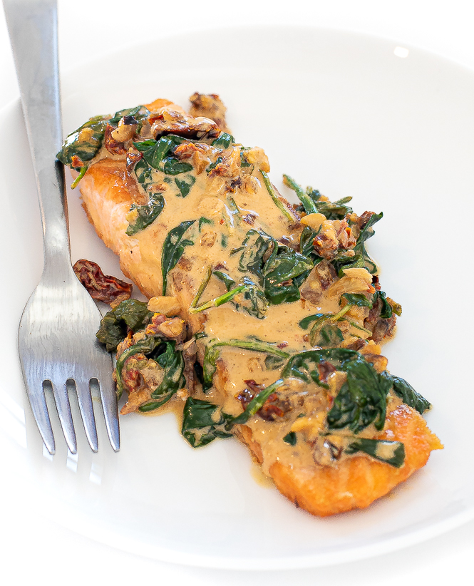 Filet of tuscan salmon on a white plate with a silver fork.