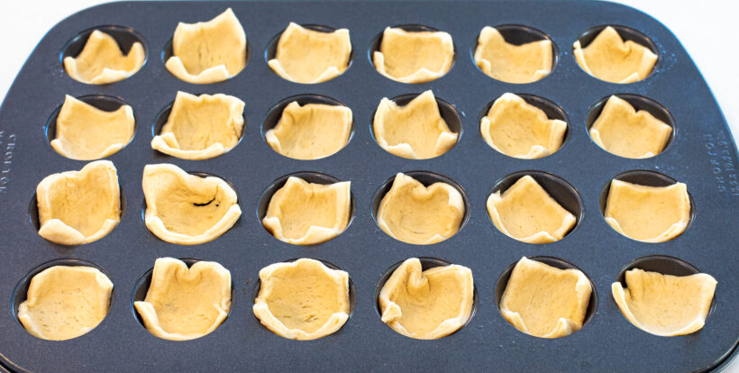 Crescent roll squares tucked into a mini muffin tin. 