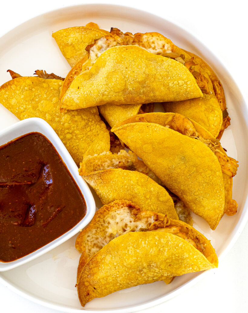 Crispy Baked Chicken Tacos on a plate next to a bowl of salsa.