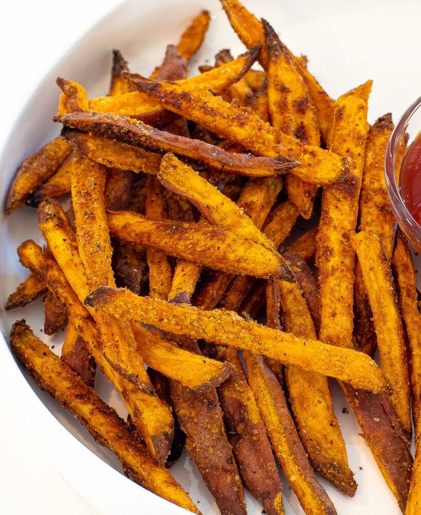 Sweet potato fries on a plate next to a small serving of spicy ketchup.