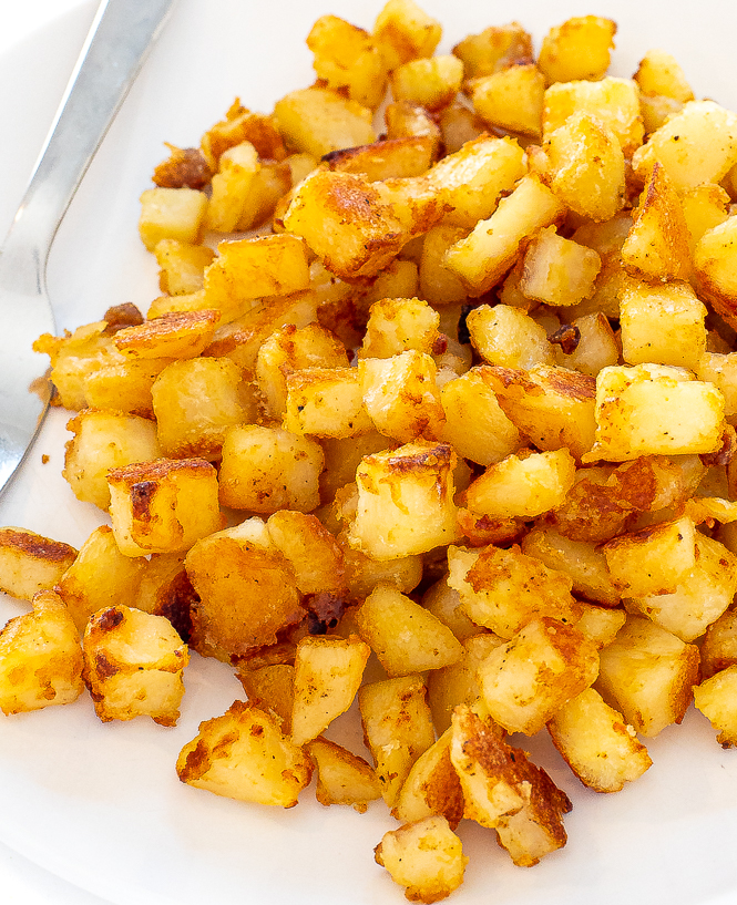 Breakfast potatoes in a white bowl with a silver fork.