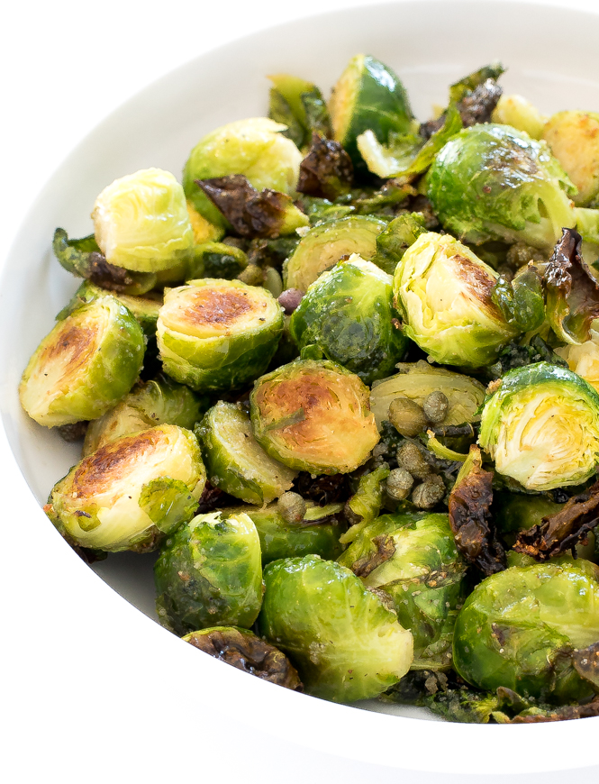 A white bowl of crispy brussels sprouts with capers.