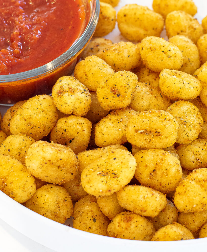 Close up shot of crispy gnocchi on a white plate with a bowl of marinara sauce on the side.
