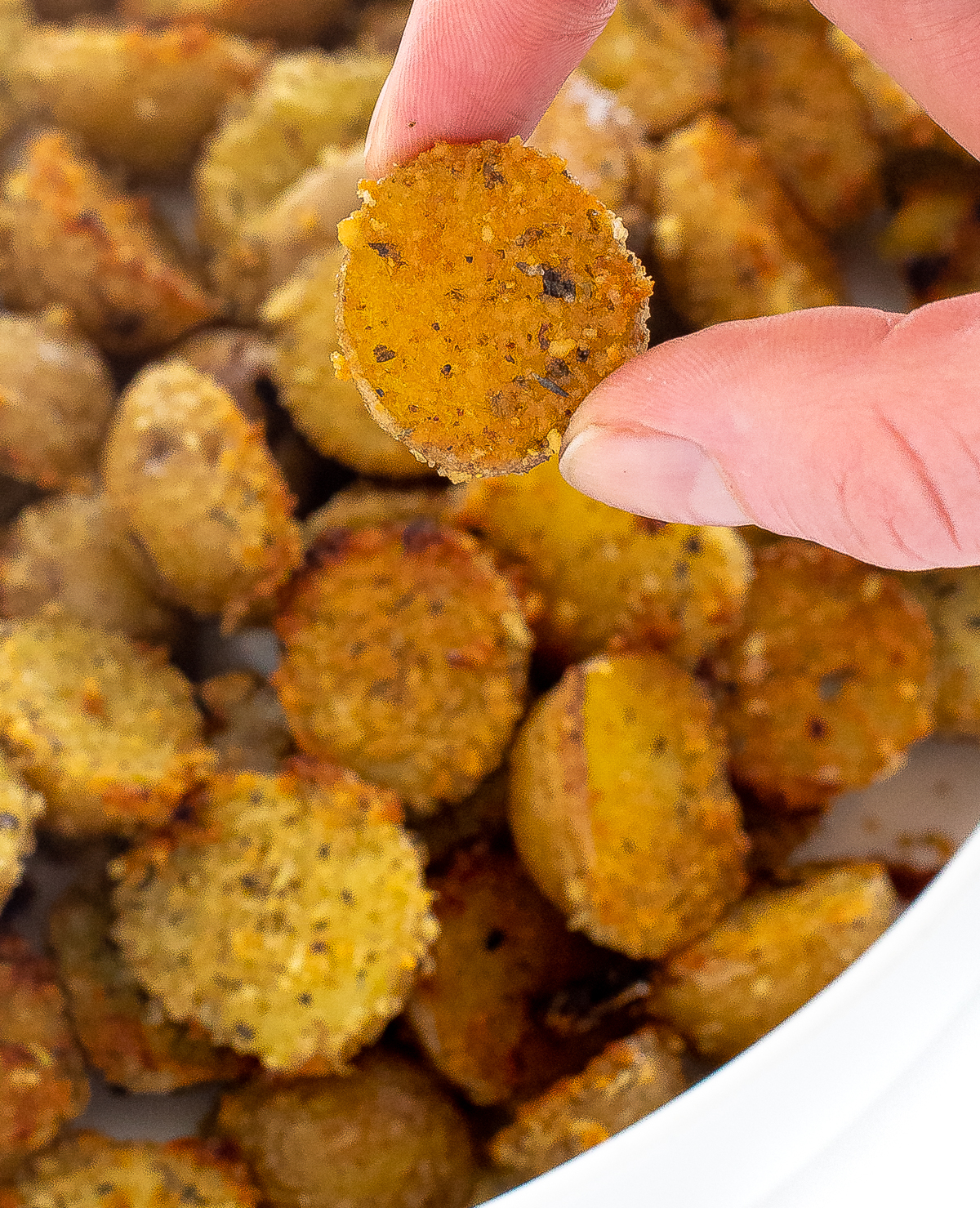 Hand holding a potato with the parmesan crusted side towards the camera and more potatoes in the background. 