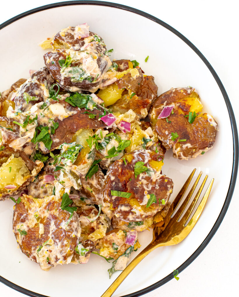 Close up of roasted potato salad on a white plate with a gold fork.