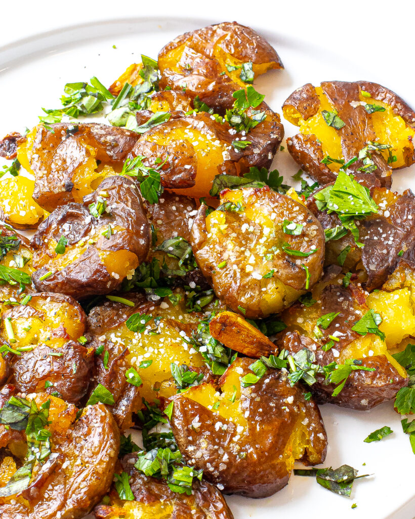 Plate full of smashed potatoes sprinkles with salt and herbs. 