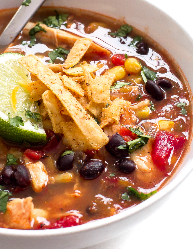 Chicken enchilada soup with lime wedge and tortilla strips in white bowl with spoon Chicken enchilada soup with lime wedge and tortilla strips in white bowl with spoon