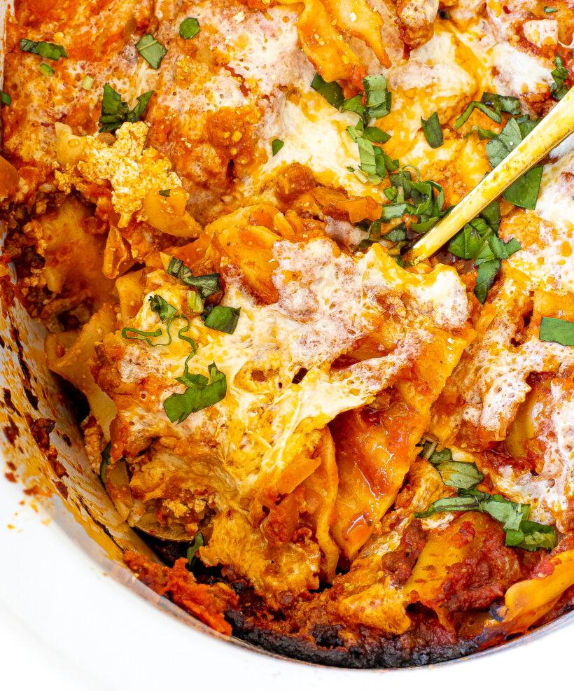 Close up view of a spoon scooping out a serving of lasagna from the slow cooker.