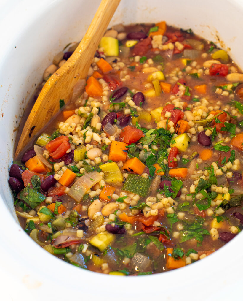 cooked minestrone soup in slow cooker with wooden spoon
