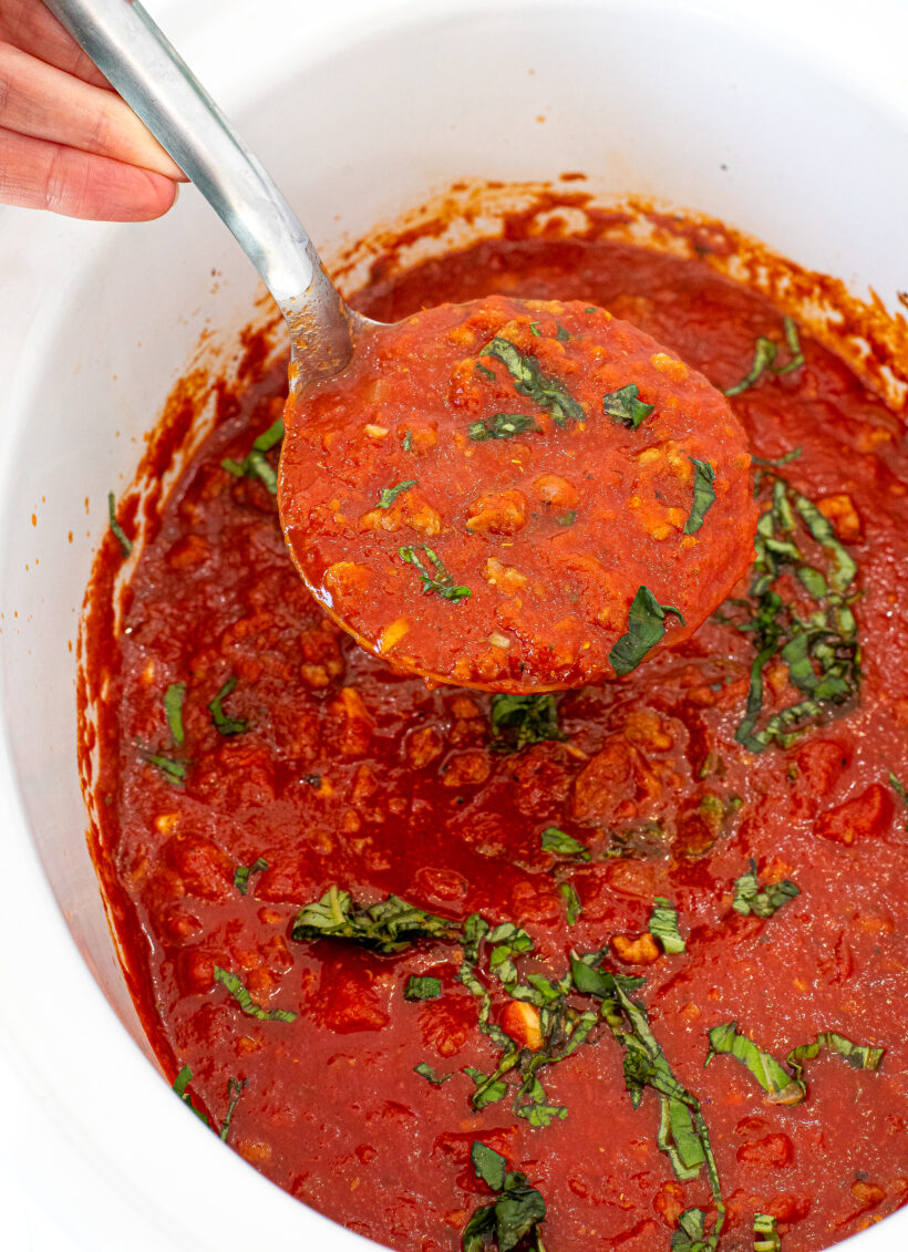 slow cooker tomato sauce in a crockpot with fresh basil on top