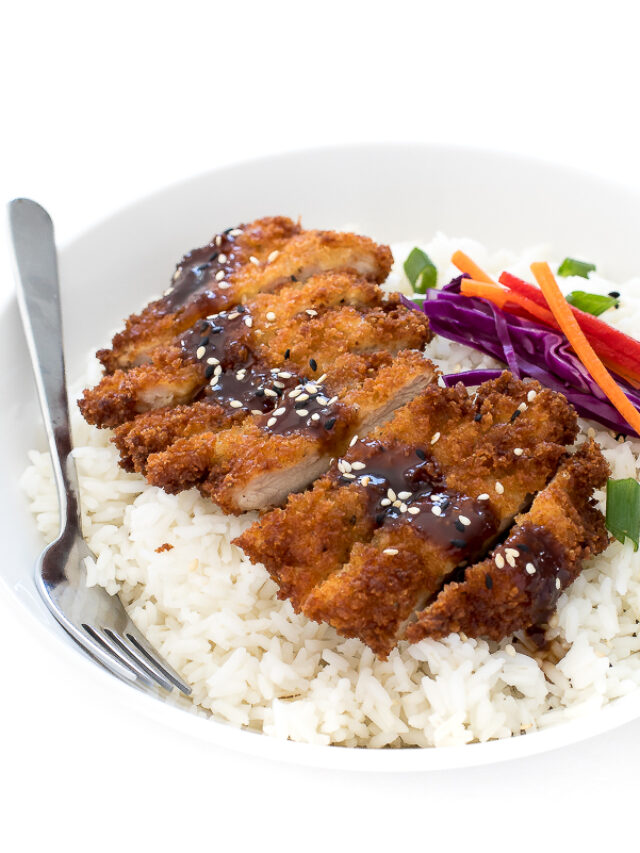 Sliced chicken katsu on a bed of white rice next to veggies.