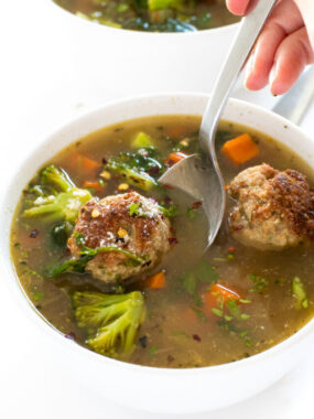 a serving of this Turkey Meatball Vegetable Soup in a white bowl with a spoon